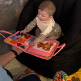 Maluch bawi się różową książeczką sensoryczną Nolinu na pufie